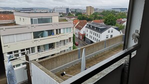 Vista des d'una finestra sobre un paisatge urbà amb edificis, un carrer i una zona industrial llunyana.