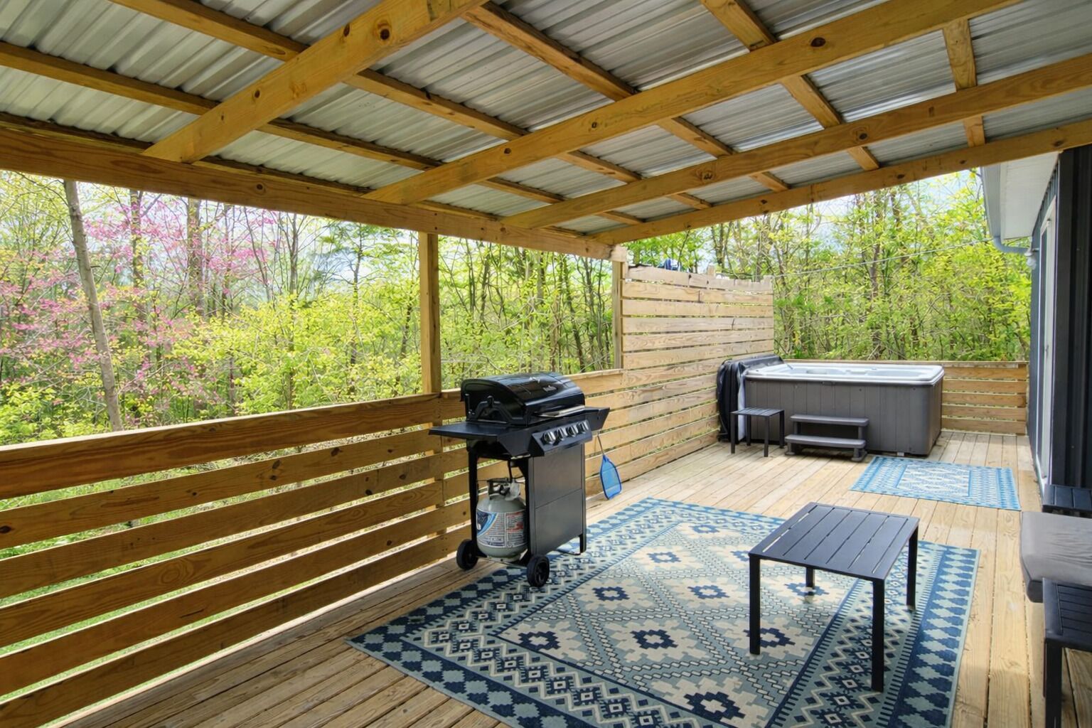 A covered outdoor area with a grill, seating, and a hot tub.