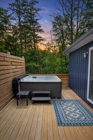 A wooden deck with a hot tub, a small table, and a rug. - Blue Bird Tiny House: Hot Tub + Rooftop Deck (Logan)