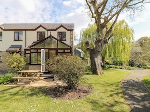 Une maison avec une véranda, un jardin avec un grand arbre et un chemin pavé.