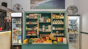 Una pequeña tienda de comestibles con una variedad de productos en estantes y congeladores, una máquina de café y un menú en una pizarra.