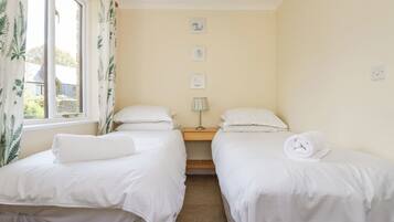 Quarto com duas camas de solteiro, mesa de cabeceira com luminária e janela com cortinas.