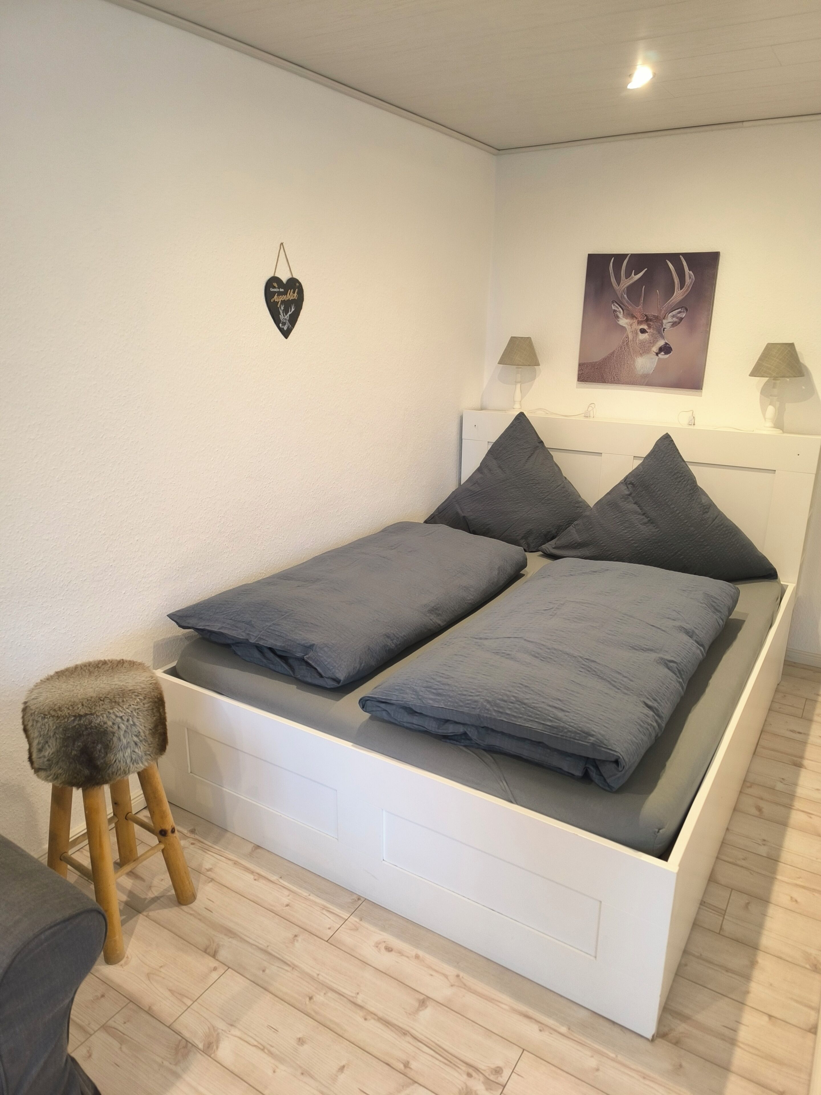Un lit avec un tiroir de rangement en dessous, un petit tabouret et deux lampes fixées au mur.