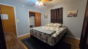 Une chambre à coucher avec un lit, un ventilateur de plafond, une porte et un tableau accroché au mur.