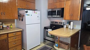 Une cuisine avec des meubles de rangement en bois, un réfrigérateur blanc, un four à micro-ondes, un four traditionnel et un plan de travail en bois.