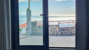 A view through a window of a coastal building with a stone wall and a flagpole. - Sandine House (Estreito da Calheta)