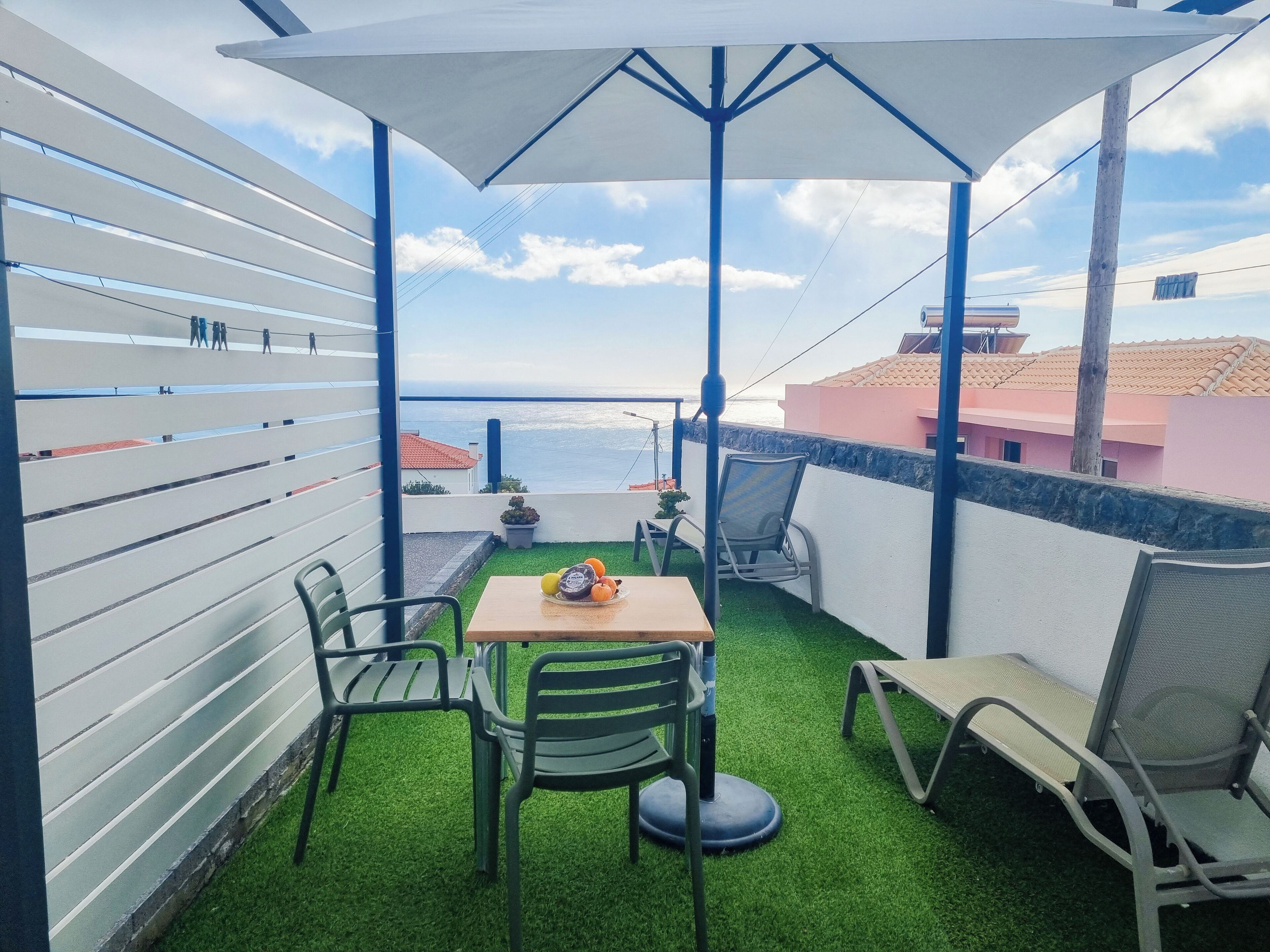 A balcony with a table, chairs, and a view of the sea.