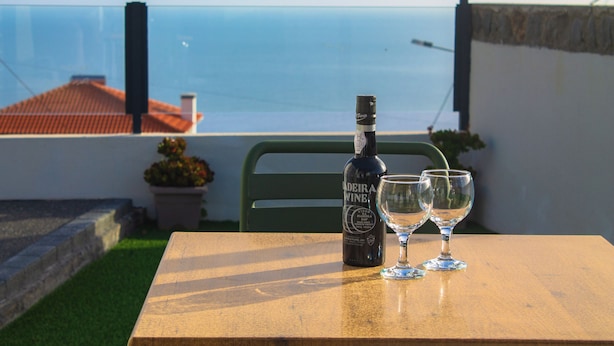 A bottle of Madeira wine and two glasses on a table with a view of the sea. - Sandine House (Estreito da Calheta)