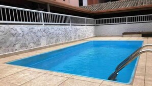 Una piscina rectangular con borde de azulejos, rodeada por una barandilla blanca y un muro de mármol.