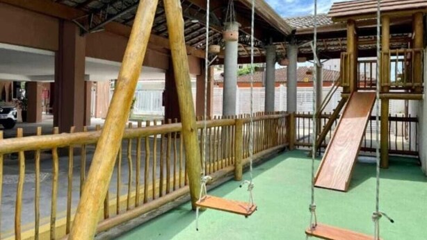 Un espacio al aire libre cubierto con cerca de madera, columpios y un tobogán.