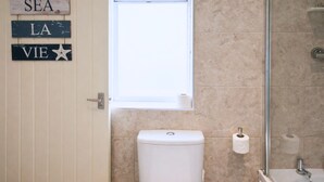 Une salle de bain comprenant des toilettes, une fenêtre et un espace douche.
