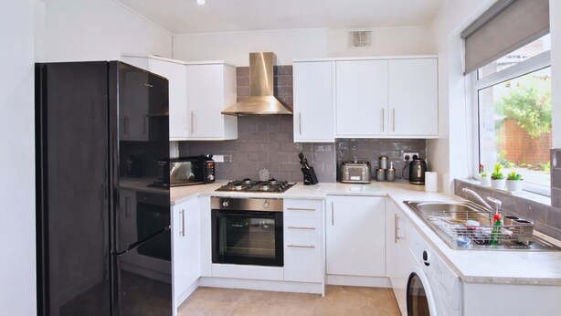 Une cuisine moderne avec des meubles blancs, un réfrigérateur noir, une cuisinière, un four et un lave-linge.