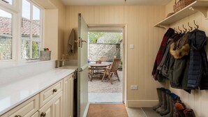 Une cuisine avec une fenêtre, un coin repas avec une table et des chaises, et un porte-manteau avec des bottes.