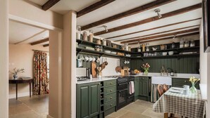 Une cuisine avec des meubles de rangement verts, une cuisinière et une table à manger recouverte d’une nappe à carreaux.