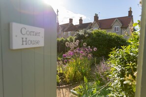 Um jardim com uma placa que diz 'Corner House' e uma casa tradicional ao fundo.