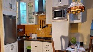 A compact kitchen with white cabinets, a built-in microwave, and a small dining area with a wooden chair and table. - Detached Terrace Cottage for Adults Only (Icod de los Vinos)