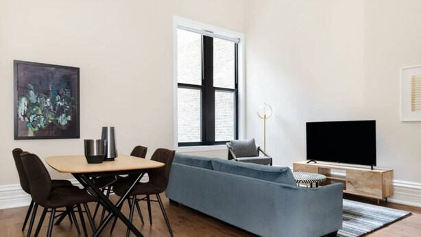 Un salon moderne comprenant un coin repas, une grande fenêtre, un téléviseur à écran plat et une œuvre d’art abstraite accrochée au mur.