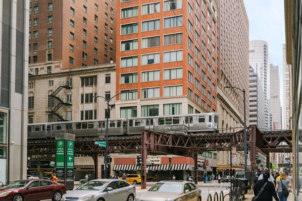 A multi-story building with a fire escape, a pedestrian bridge, and a train on an elevated track.