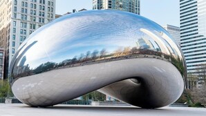 Une grande sculpture métallique aux reflets brillants, située dans un environnement urbain.