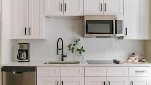 Une cuisine moderne avec des meubles blancs, un lave-vaisselle en acier inoxydable, une machine à café, un four à micro-ondes et une plante posée sur le plan de travail.