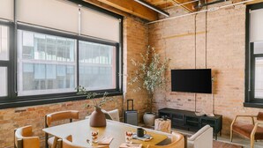A dining area with a brick wall, a television mounted on the wall, and a large window.