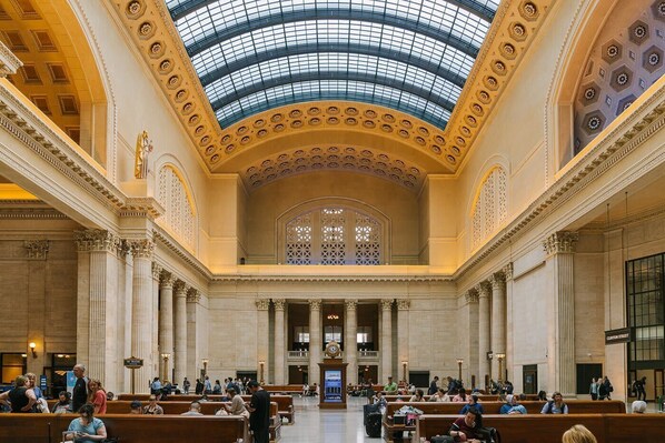 A spacious lobby with high ceilings and a skylight, featuring marble columns and a central staircase.
