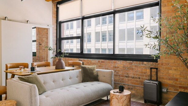 A modern room with a sofa, a dining table, and a window with a view of buildings.
