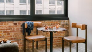 A cozy dining area with a round table and two chairs, a brick wall, and a window with a view of buildings. - LIVN West Loop Chicago King Studio (Chicago)