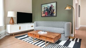 A living room with a grey sofa, a white cabinet with a flat-screen TV, a wooden coffee table, and a black and white striped rug. - LIVN Millennium Park Downtown Chicago Superior 1BR (Chicago)