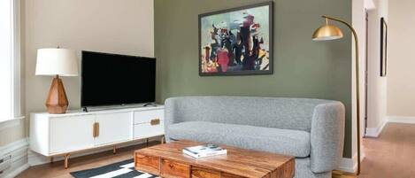 Un salon avec un canapé gris, un meuble blanc sur lequel est posée une télévision à écran plat, une table basse en bois et un tapis rayé noir et blanc.