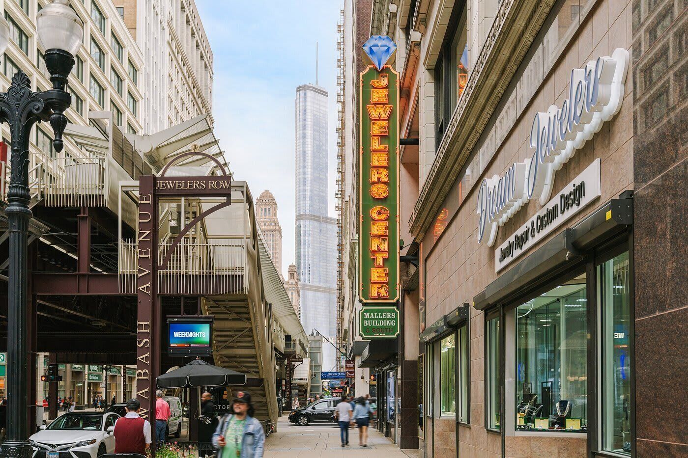 A street view with a prominent sign for the JW Marriott Center, a modern building with glass facade, and a jewelry store with a display window.