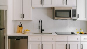 A modern kitchen with white cabinets, a stainless steel refrigerator, a dishwasher, a black faucet, a microwave, and a countertop with a knife block and bowls. - LIVN Millennium Park Downtown Chicago Superior 1BR (Chicago)