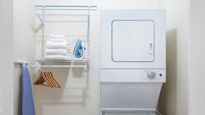 A compact laundry room with a built-in washer and dryer, a metal shelf with towels and an iron, and a blue towel hanging on a rack.