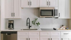 Une cuisine moderne avec des meubles blancs, un lave-vaisselle en acier inoxydable, une machine à café, un four à micro-ondes et une plante posée sur le plan de travail.