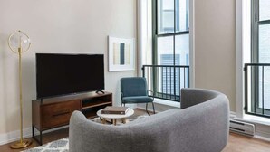 Een moderne woonkamer met een grote flatscreen televisie, een blauwe stoel, een grijze bank en een vloerlamp.