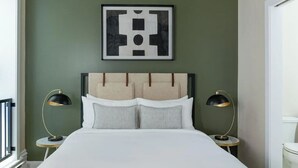 Een net opgemaakt bed met hoofdbord, twee bedlampjes en een lijst met abstracte kunst aan de muur.