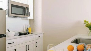 Een keuken met witte kastjes, een magnetron, een spoelbak en een aanrecht met een fles, glazen en sinaasappels.