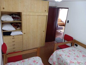 A bedroom with a wooden wardrobe, two single beds with floral bedding, a red chair, and a mirror on the wall. - JJVargas Apartment: Vive Claro, Movistar Arena, Campin, Salitre Mágico, Embassy (Bogotá)