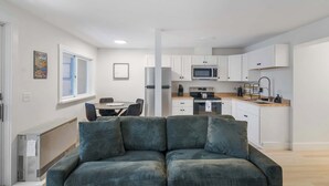 A modern apartment with a living area featuring a green sofa, a dining table, and a kitchen with white cabinets and appliances.