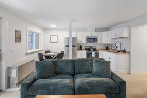 Un apartamento moderno con sala de estar que incluye un sofá verde, una mesa de comedor y una cocina con gabinetes y electrodomésticos blancos.