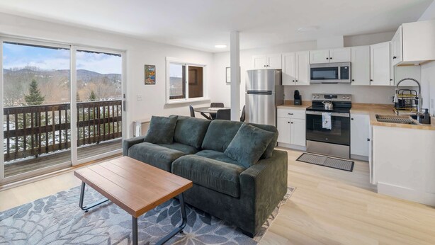 A modern apartment with a balcony, a kitchenette, a sofa, and a dining area.