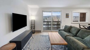 A modern living room with a flat-screen TV, a sofa, a wooden coffee table, and a patterned rug.