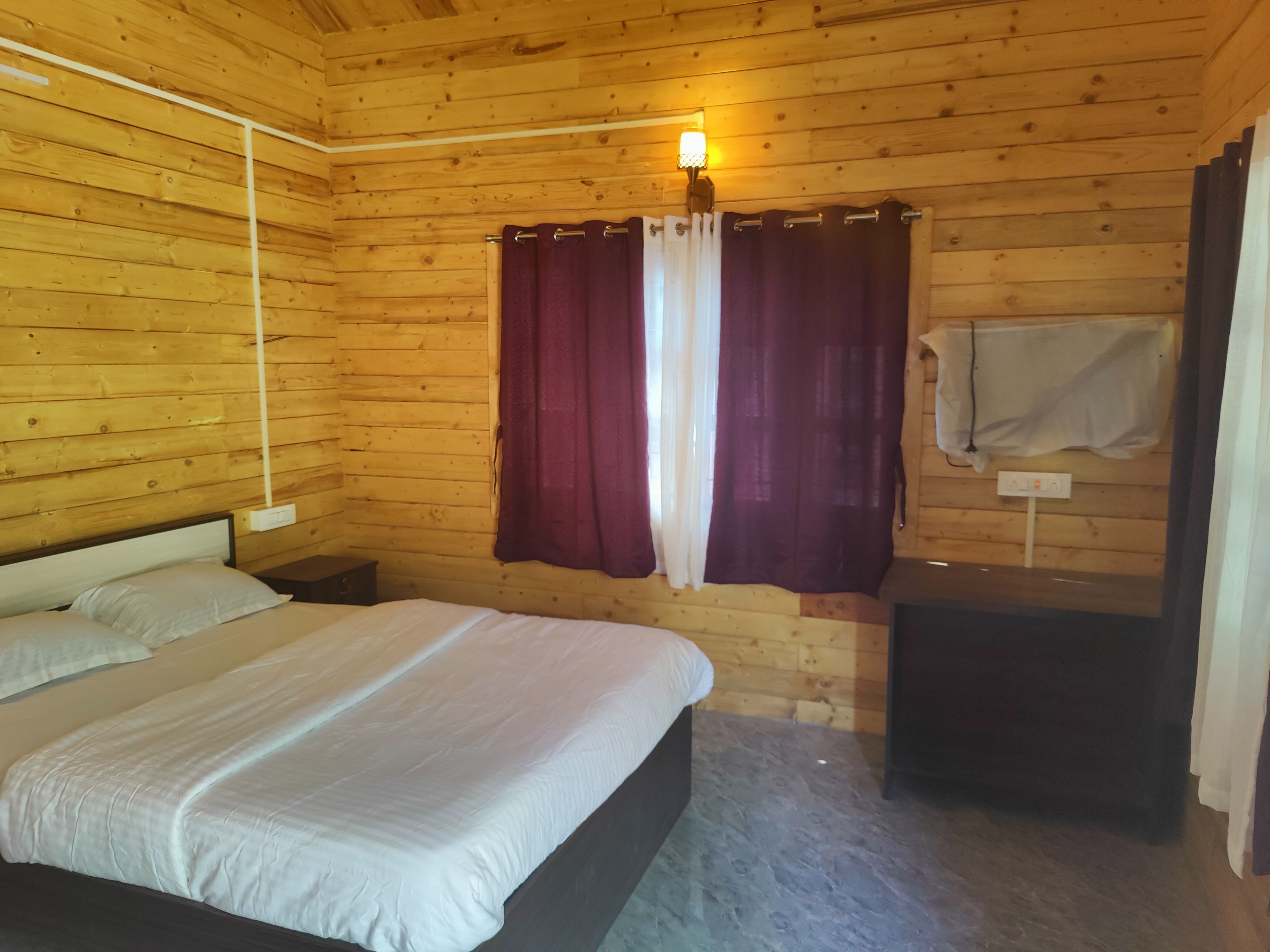 A wooden-paneled room with a bed, a nightstand, a wall-mounted lamp, and a towel hanging on a hook.