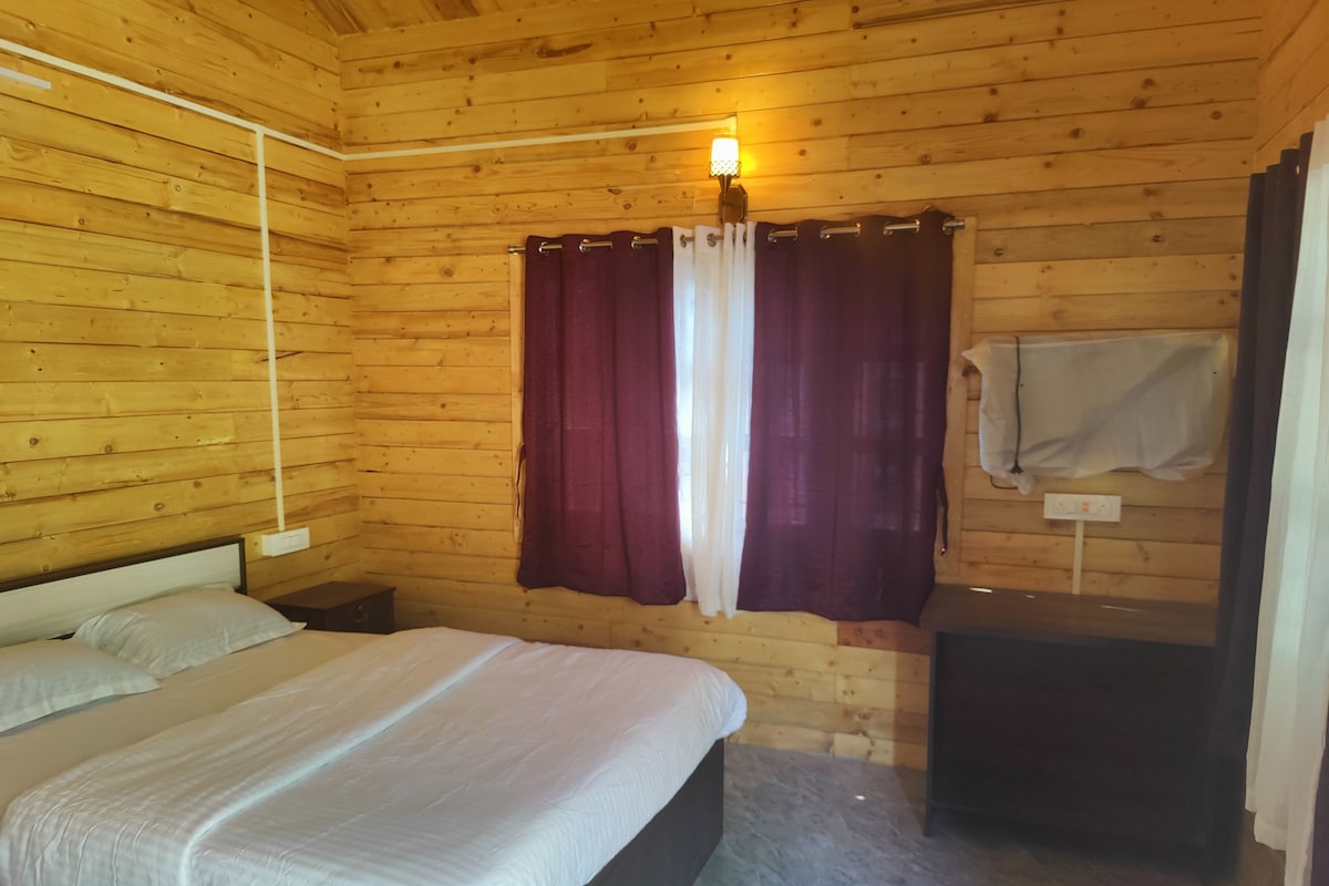 Una habitación con paneles de madera, una cama, una mesita de noche, una lámpara de pared y una toalla colgada de un gancho.