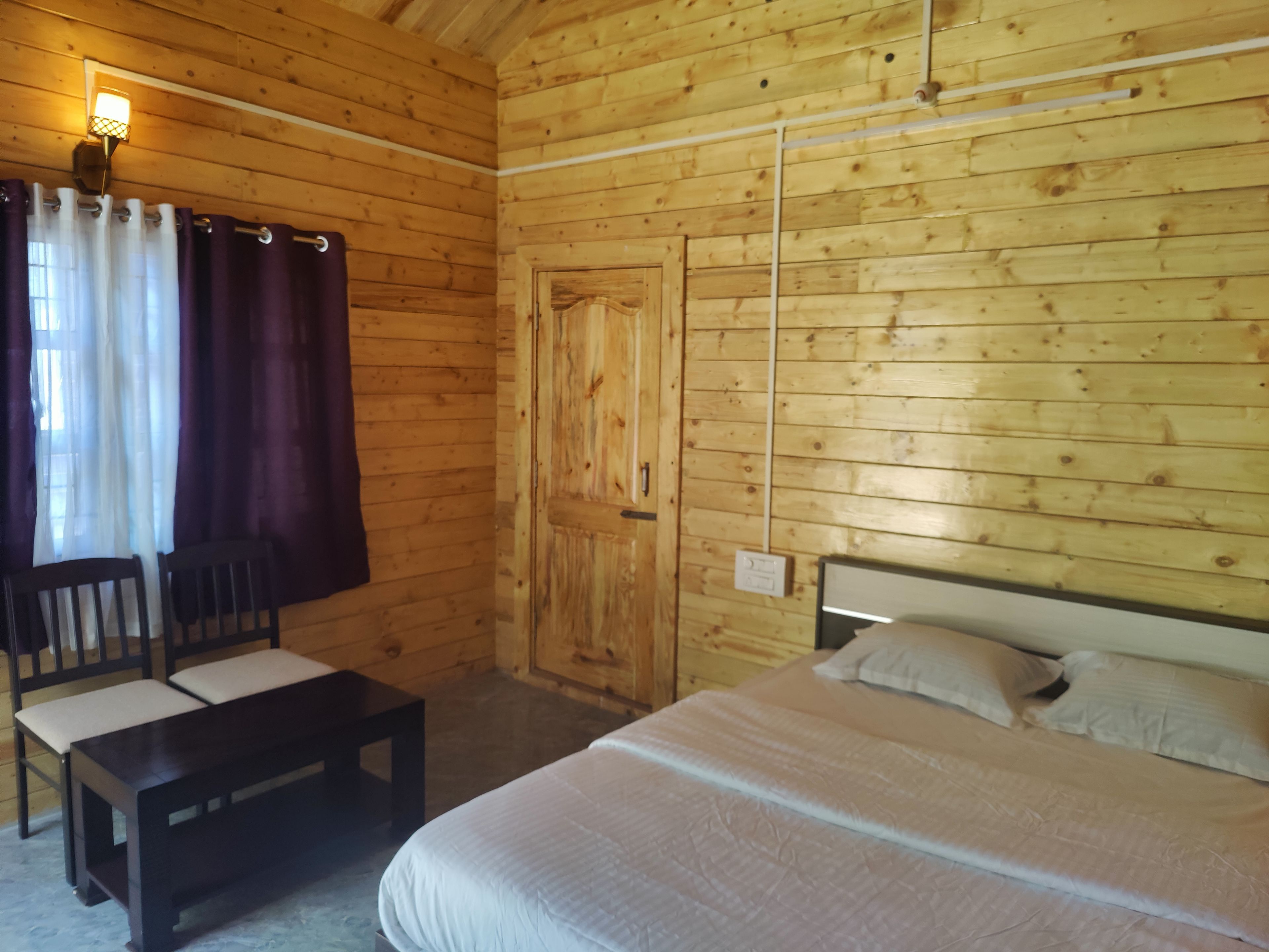 Una habitación de madera con una cama, un banco y una puerta.