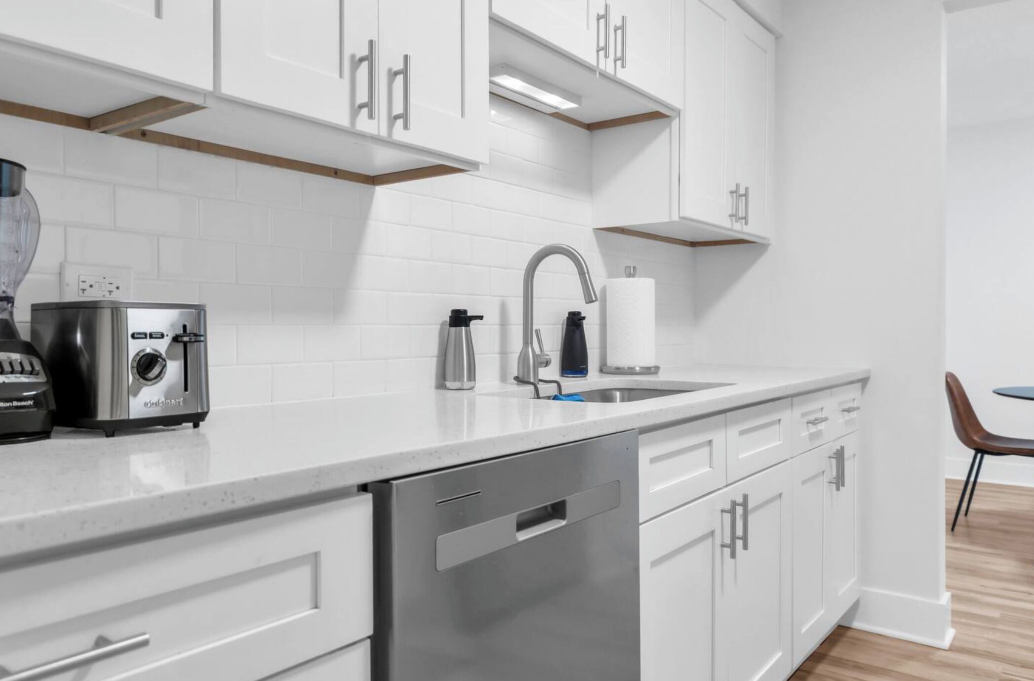 Une cuisine moderne avec des meubles blancs, un lave-vaisselle en acier inoxydable, un grille-pain et un évier avec un robinet.