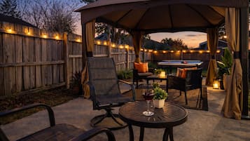 An outdoor patio area with a covered seating area, a pool table, and string lights.