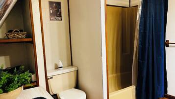 Ein Badezimmer mit Toilette, einer Duschkabine, einem Korb auf einem Regal und einem Schild an der Wand.
