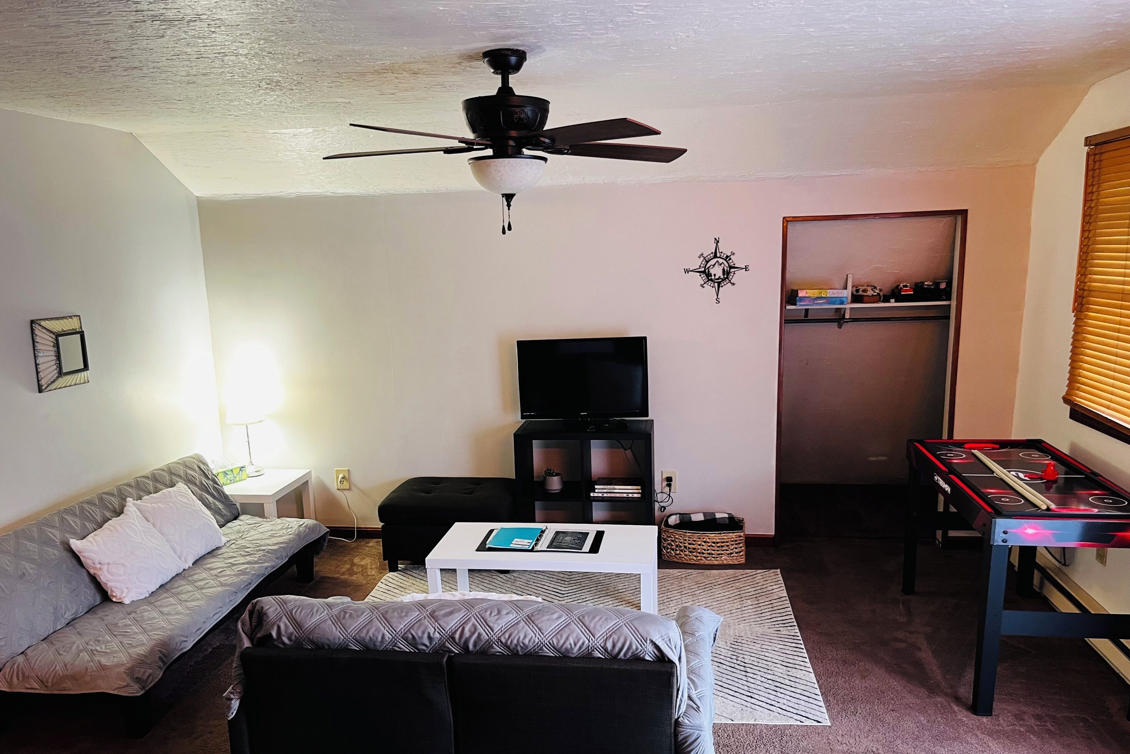 A living room with a sofa, a coffee table, a television, a ceiling fan, and a foosball table.