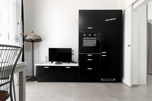 A modern kitchen with a black cabinet labeled "Manateresa," a flat-screen TV, and a patterned floor lamp. - Heart in Home - One Bedroom Apartment, Sleeps 2 (Monopoli)